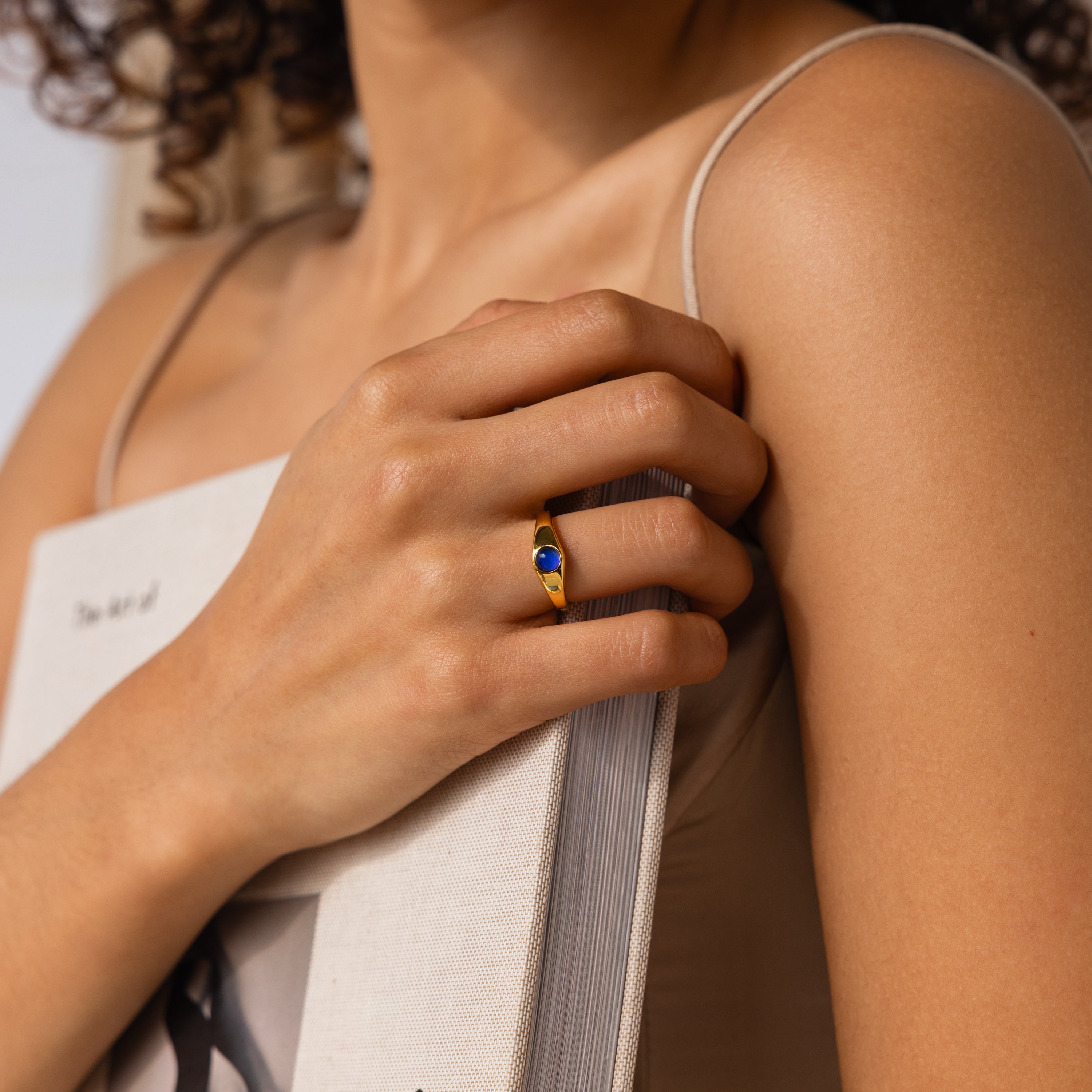 A person holding a book, wearing the Signet Mood Ring with a blue color-changing stone on their finger.