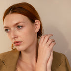 Woman with red hair wearing a brown blazer, pearl earring, Pink Baguette Opal Studs, and multiple ear piercings, looking to the side.