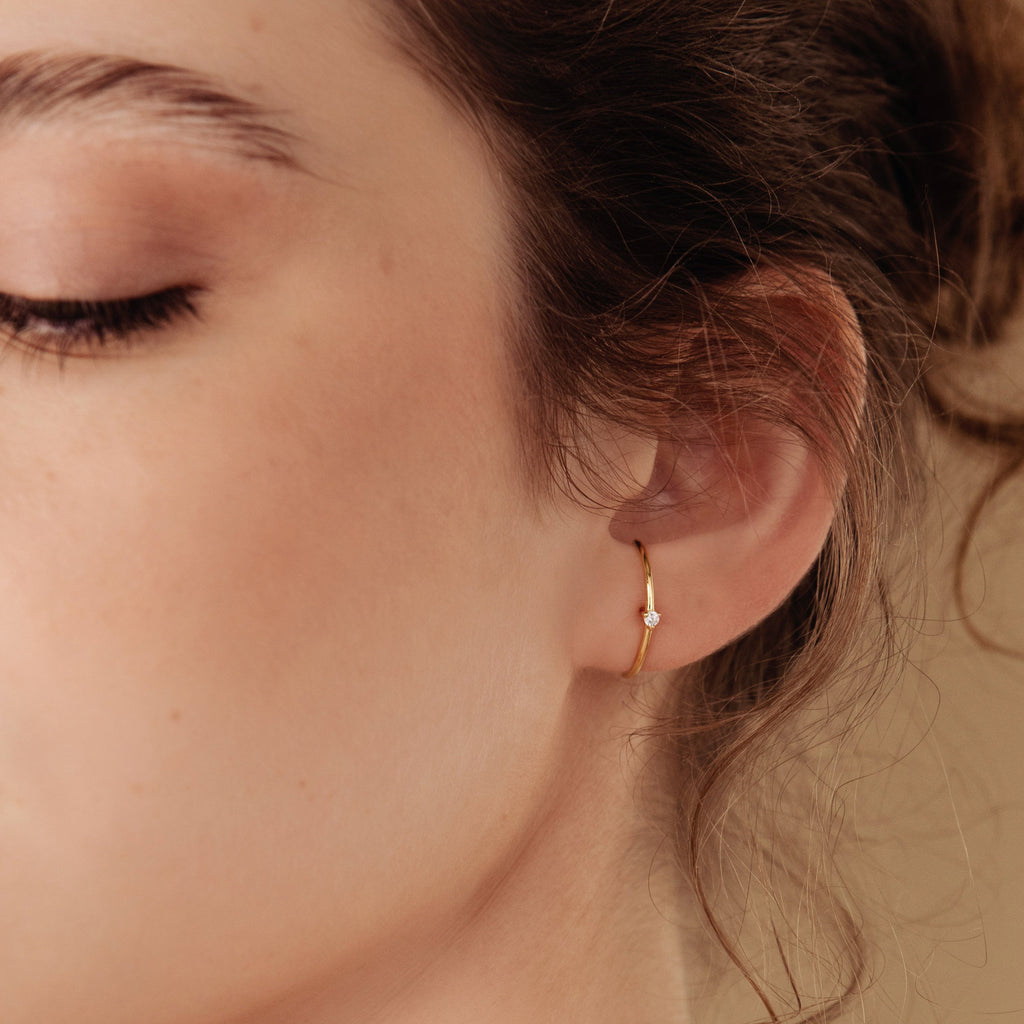 Close-up of a woman's ear wearing a gold hoop jacket earring with a diamond.