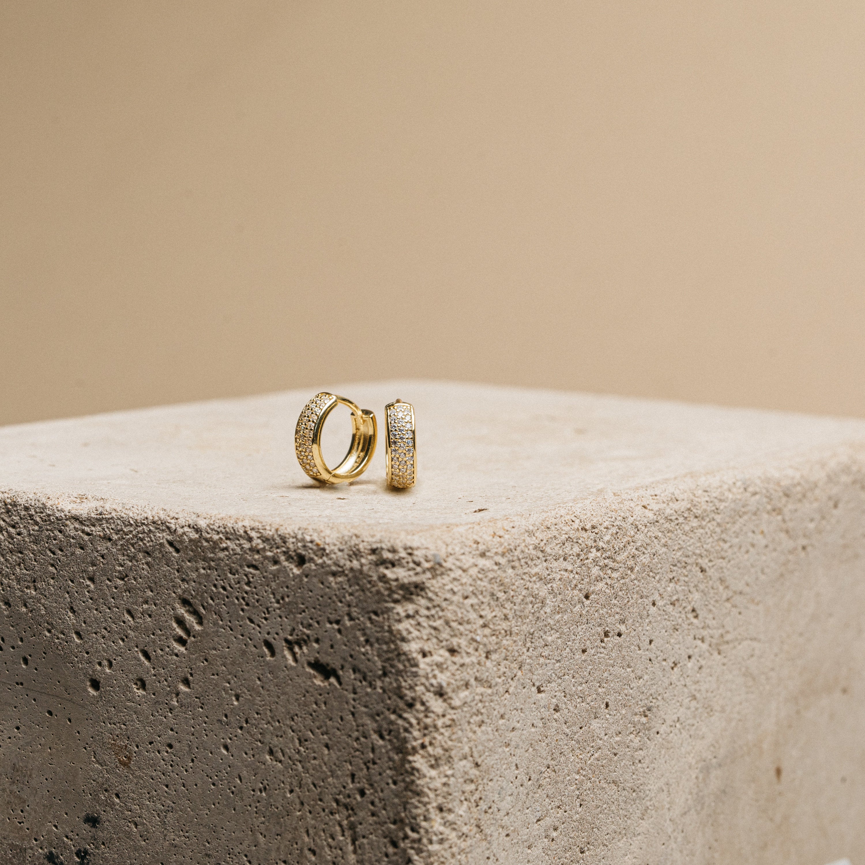 Gold hoop earrings on a textured stone surface with a beige background