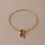 The Cross & Heart Charm Bracelet features a minimalist gold paperclip chain with delicate cross and heart pendants, beautifully displayed on a beige background.