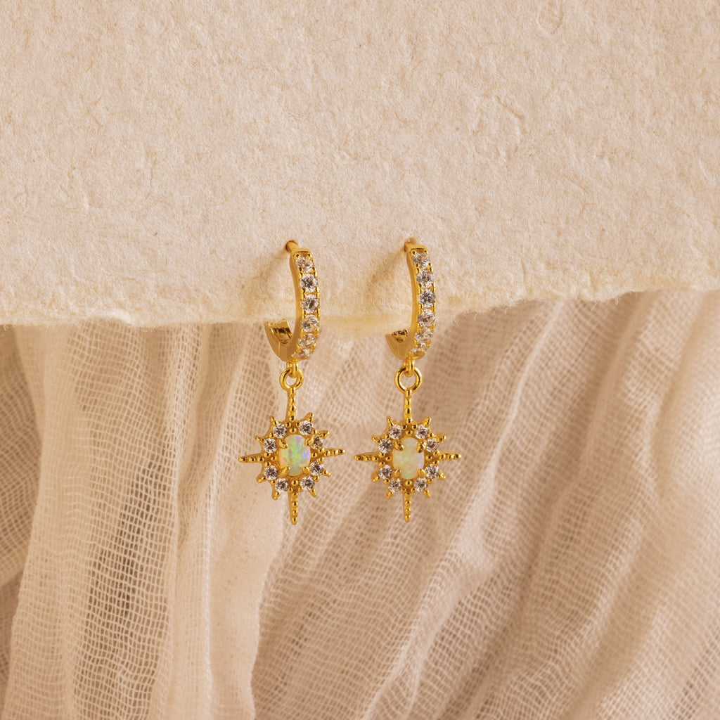 The Opal Star Necklace & Earrings Set in 18K Gold features sun-inspired opal pendants and hoops, displayed on textured beige fabric. Pair this radiant set for a coordinated, elegant look.