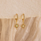 The Opal Star Necklace & Earrings Set in 18K Gold features sun-inspired opal pendants and hoops, displayed on textured beige fabric. Pair this radiant set for a coordinated, elegant look.