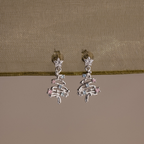 Silver Christmas tree earrings with gemstones on a beige fabric background