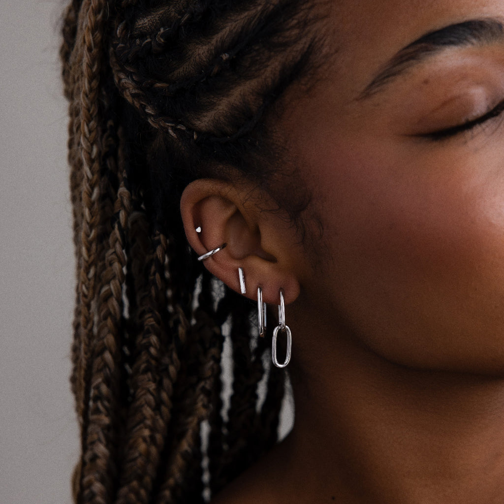 Close-up of a women's ear with multiple silver earrings against a neutral background