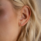 A silver pear opal stud worn on a woman’s earlobe, subtly catching the light for a soft, iridescent glow.