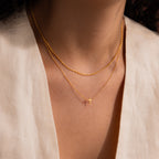 Model wearing a dainty gold cross charm necklace, layered with a gold mariner chain necklace.