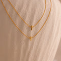 Two dainty gold cross charm necklaces in 16 and 18 inches, displayed against a neutral stone surface.