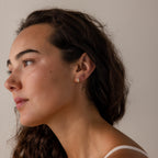 Woman with wavy brown hair wearing Diamond Heart Hoops earrings, looking to the left against a plain background.