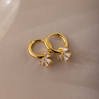 Gold Diamond Bow Hoop Earrings with delicate cubic zirconia bows, styled flat on a neutral taupe background.