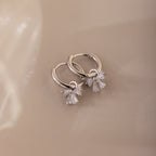Close-up of silver hoop earrings with diamond-studded bow charms, displayed on a neutral background.