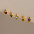 The Birthstone Heart Hoops by Caitlyn Minimalist feature heart-shaped gemstones in various colors, each accented with a clear stone—ideal for pairing with your favorite birthstone earrings or diamond huggies for a coordinated look.