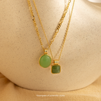 Mystery Jewelry: Two gold necklaces with green gemstone pendants displayed on a cream surface, offering whimsical charm—ideal for anyone seeking unique, intriguing accessories.