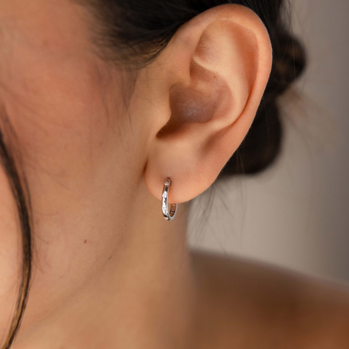 Close-up of an ear wearing our Classic Diamond Sprinkle Huggie earring with a neutral background