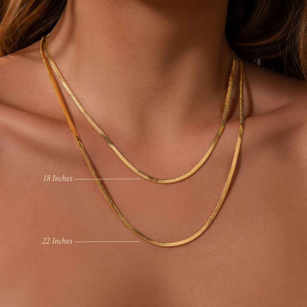 Close-up of a woman wearing two Bold Snake Chain Necklaces in gold—one 18 inches and one 22 inches—layered on her collarbone for a modern, elegant jewelry look.