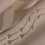 Two floral chain diamond bracelets in gold and silver on a beige background