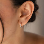 Close-up of an ear wearing a silver hoop earring with a neutral background