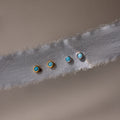Two pairs of gold and silver earrings with turquoise stones on a textured fabric background