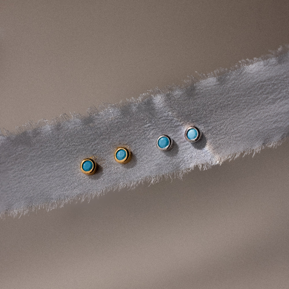Two pairs of gold and silver earrings with turquoise stones on a textured fabric background