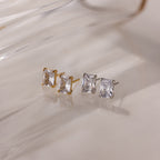 Two pairs of gold and silver stud earrings with clear gemstones on a light background