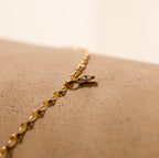 A Dainty Marquise Pendant Necklace in 18K Gold is displayed on a textured beige surface.