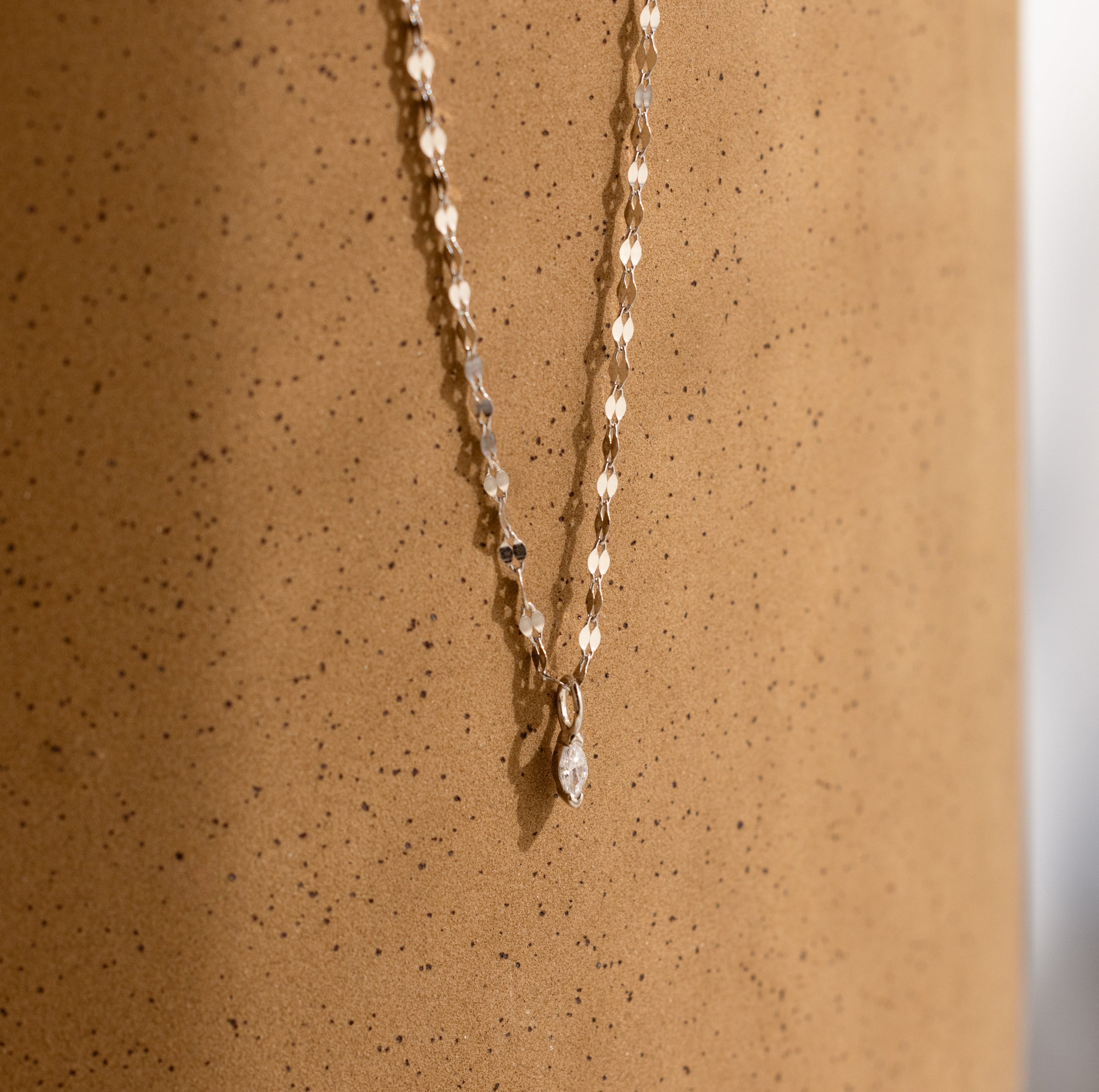 Dainty Marquise Pendant Necklace in Silver with a mirror twist chain, displayed elegantly against a speckled, light brown cylindrical surface.