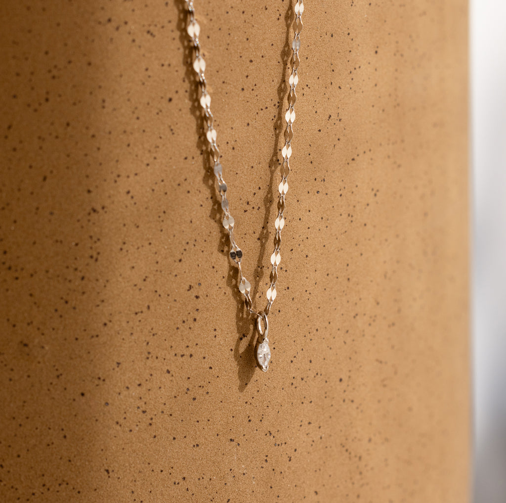 The Dainty Marquise Pendant Necklace is shown against a speckled beige background.