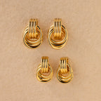 Flat lay of two pairs of Triple Knot Earrings—one larger, one mini—displayed on a textured beige background.
