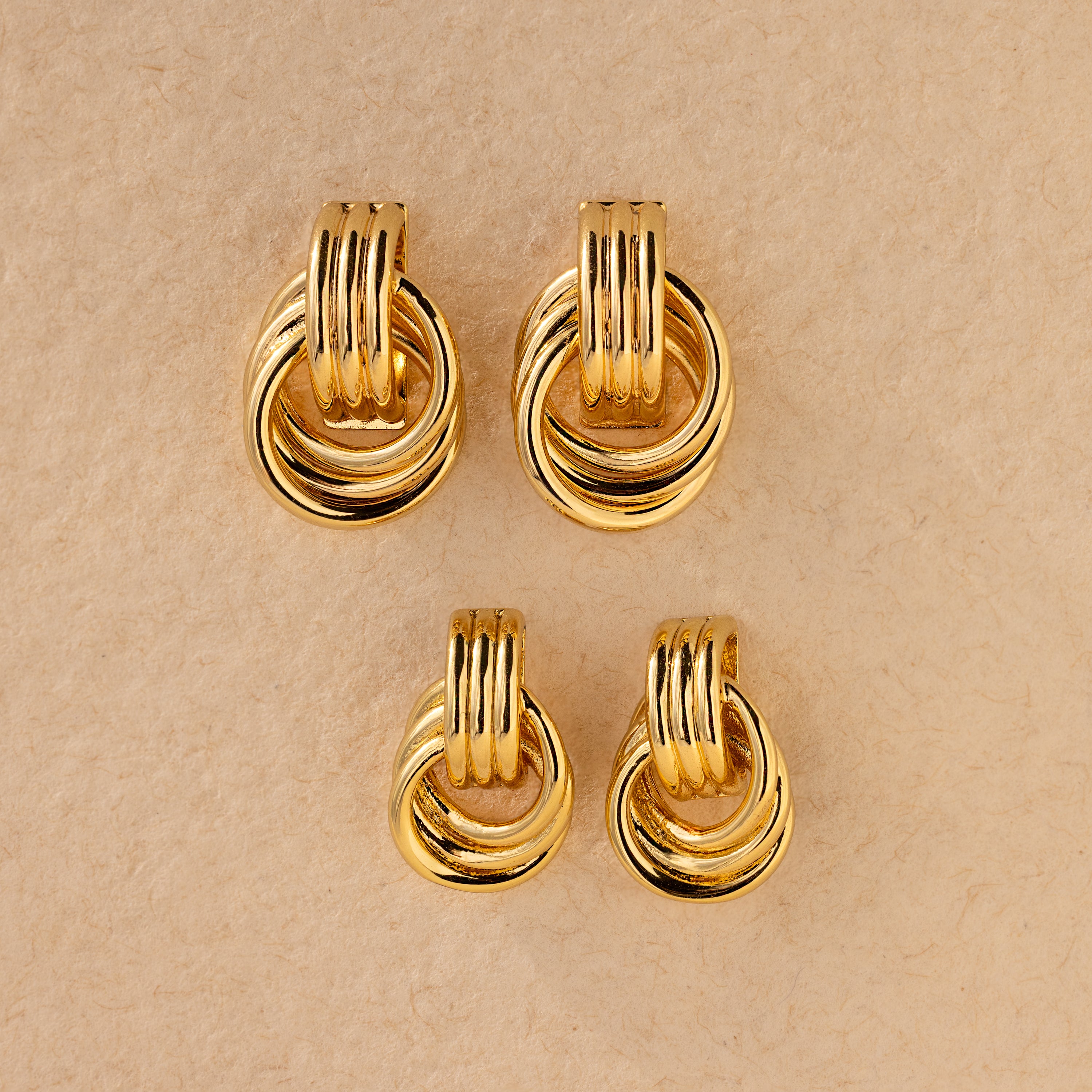 Flat lay of two pairs of Triple Knot Earrings—one larger, one mini—displayed on a textured beige background.