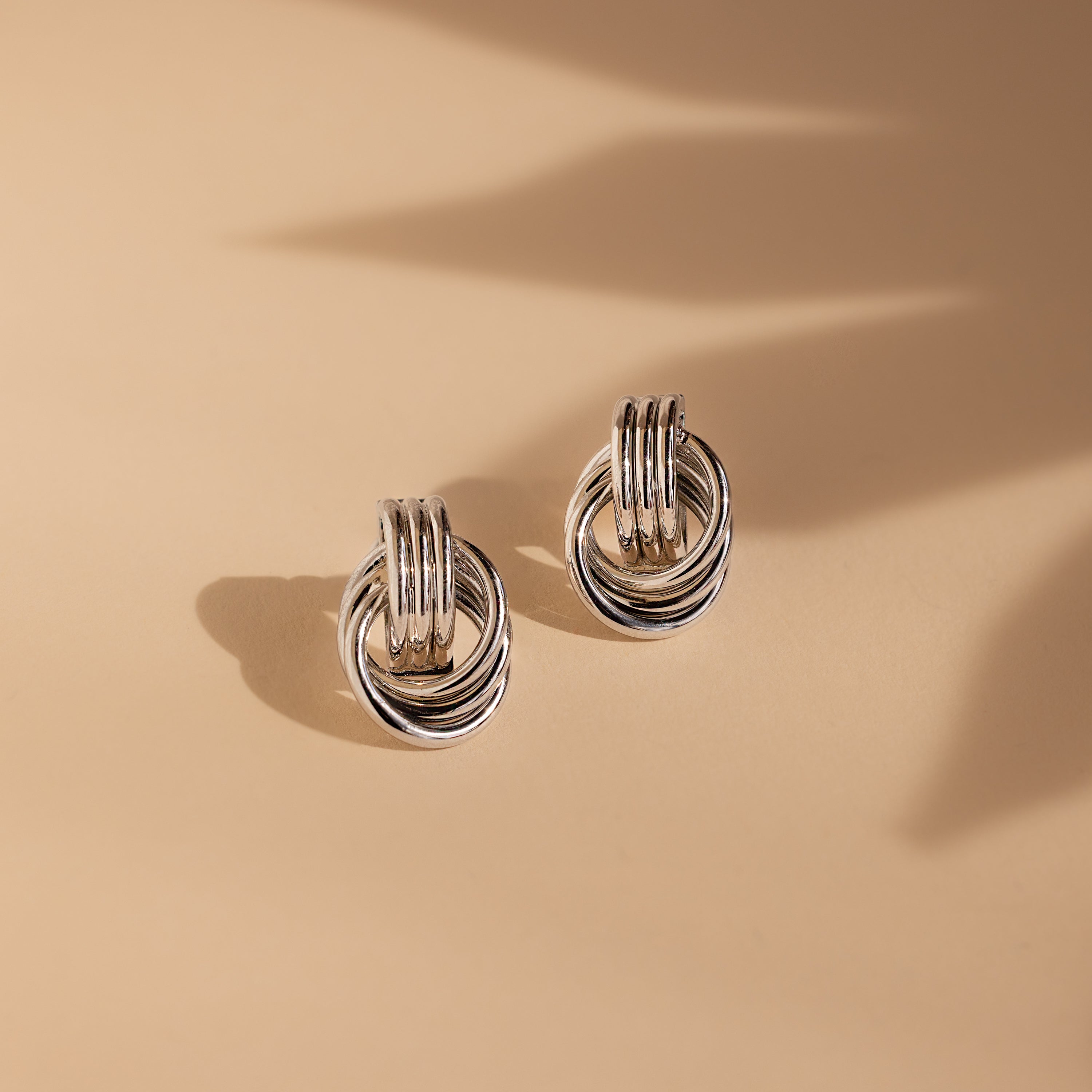 Triple Knot Earrings displayed on a beige surface with soft shadows—these elegant earrings are an ideal anniversary gift.