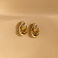 A pair of Mini Triple Knot Earrings in gold displayed upright on a smooth, neutral-toned surface.