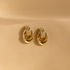 A pair of Mini Triple Knot Earrings in gold displayed upright on a smooth, neutral-toned surface.