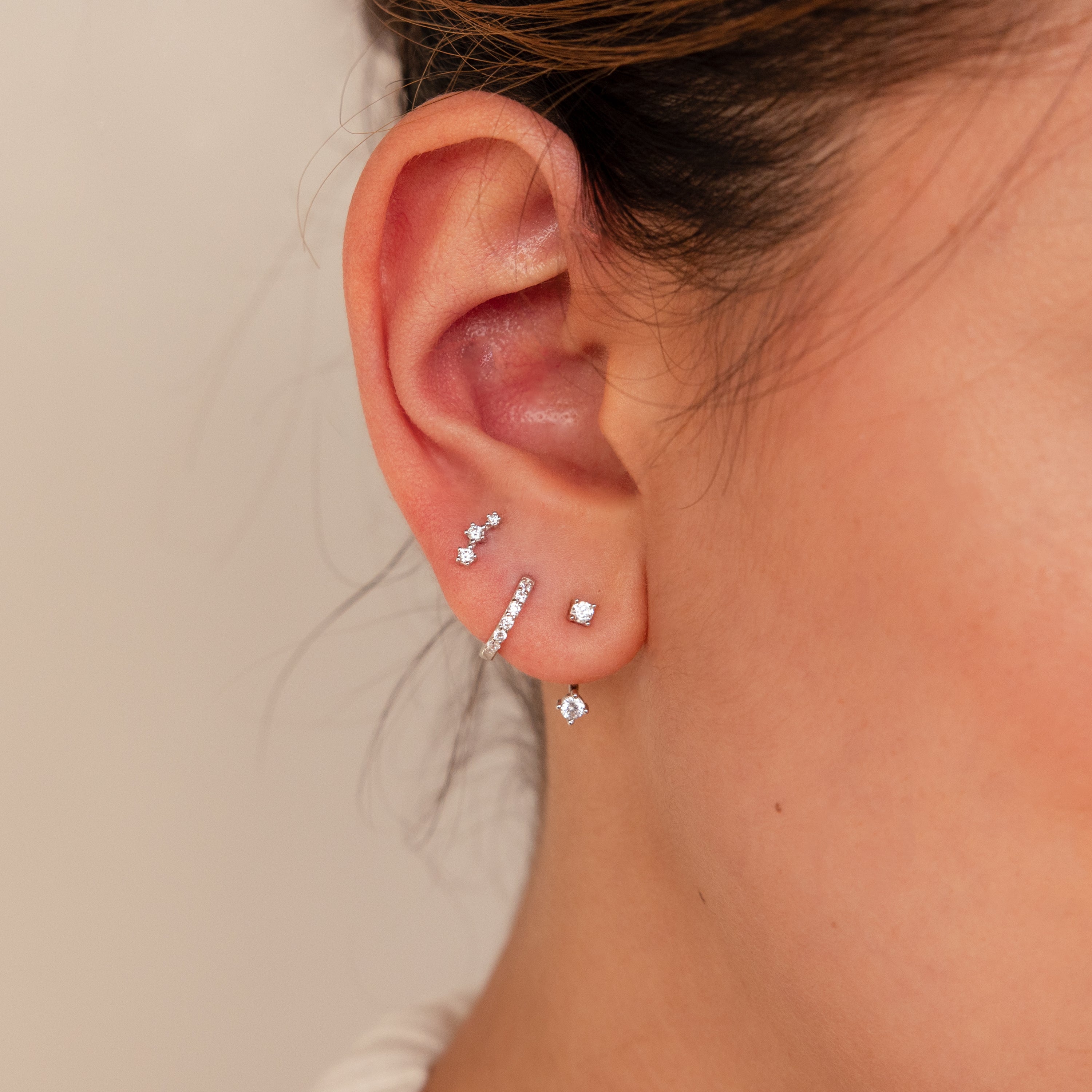 Close-up of an ear with multiple piercings, each adorned with the Diamond Earrings Set in Sterling Silver, featuring sparkling huggie hoops and dainty studs.