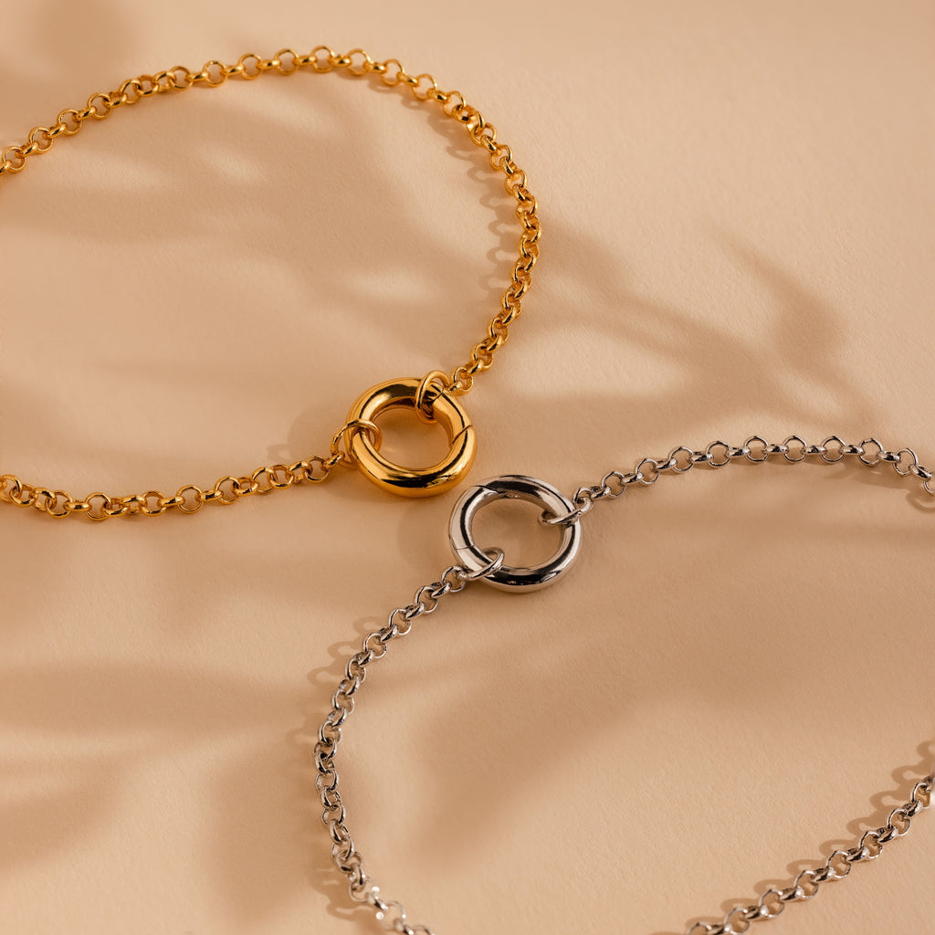 The Rolo Circle Charm Bracelet in White Gold features a detachable hinged circle clasp, perfect for minimalist style or adding charms, and is displayed elegantly on a beige surface.
