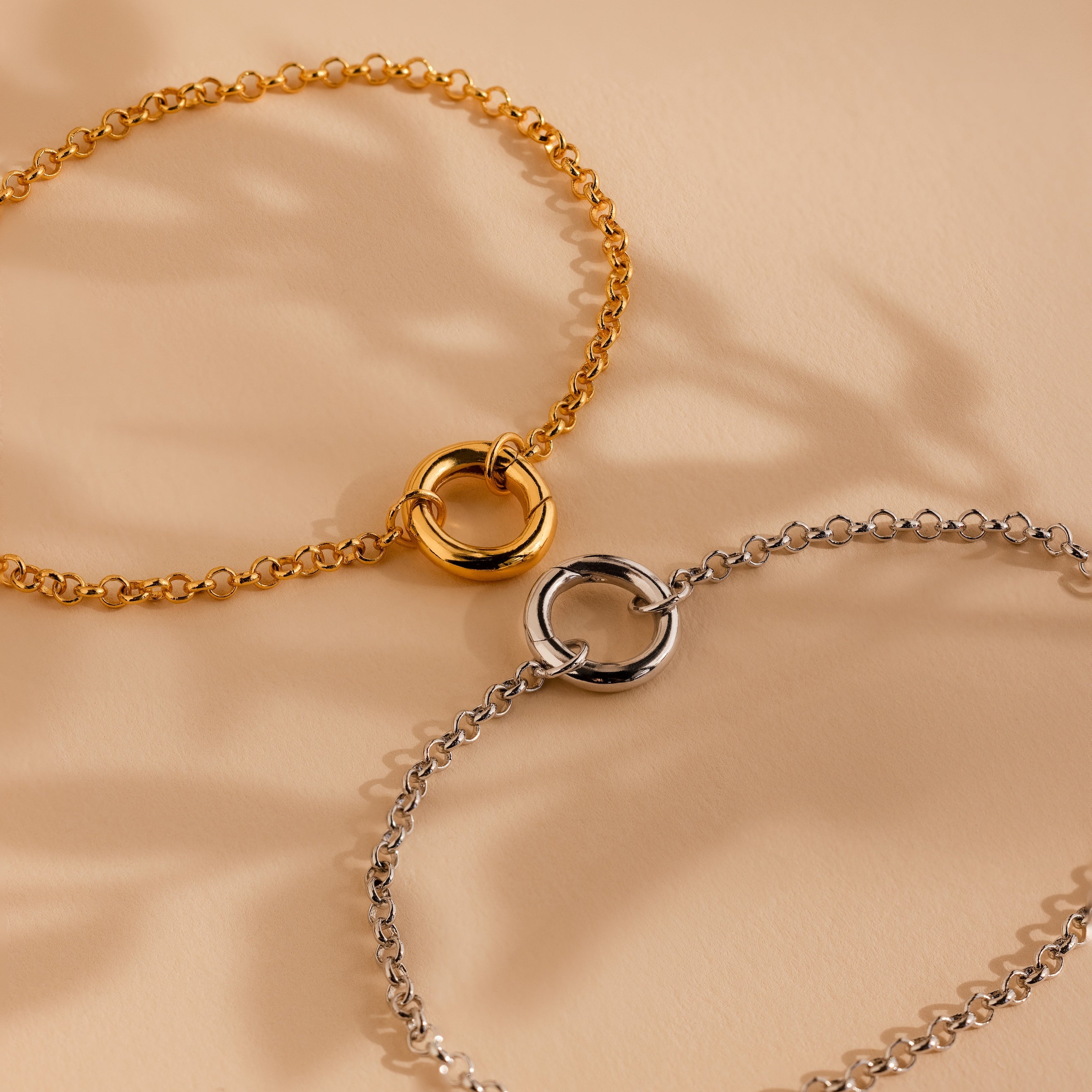 The Rolo Circle Charm Bracelet in White Gold features a detachable hinged circle clasp, perfect for minimalist style or adding charms, and is displayed elegantly on a beige surface.