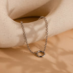 The Rolo Circle Charm Bracelet in White Gold features a detachable hinged circle, ideal for adding your own charms or achieving a minimalist style—shown on a textured, neutral-toned surface.