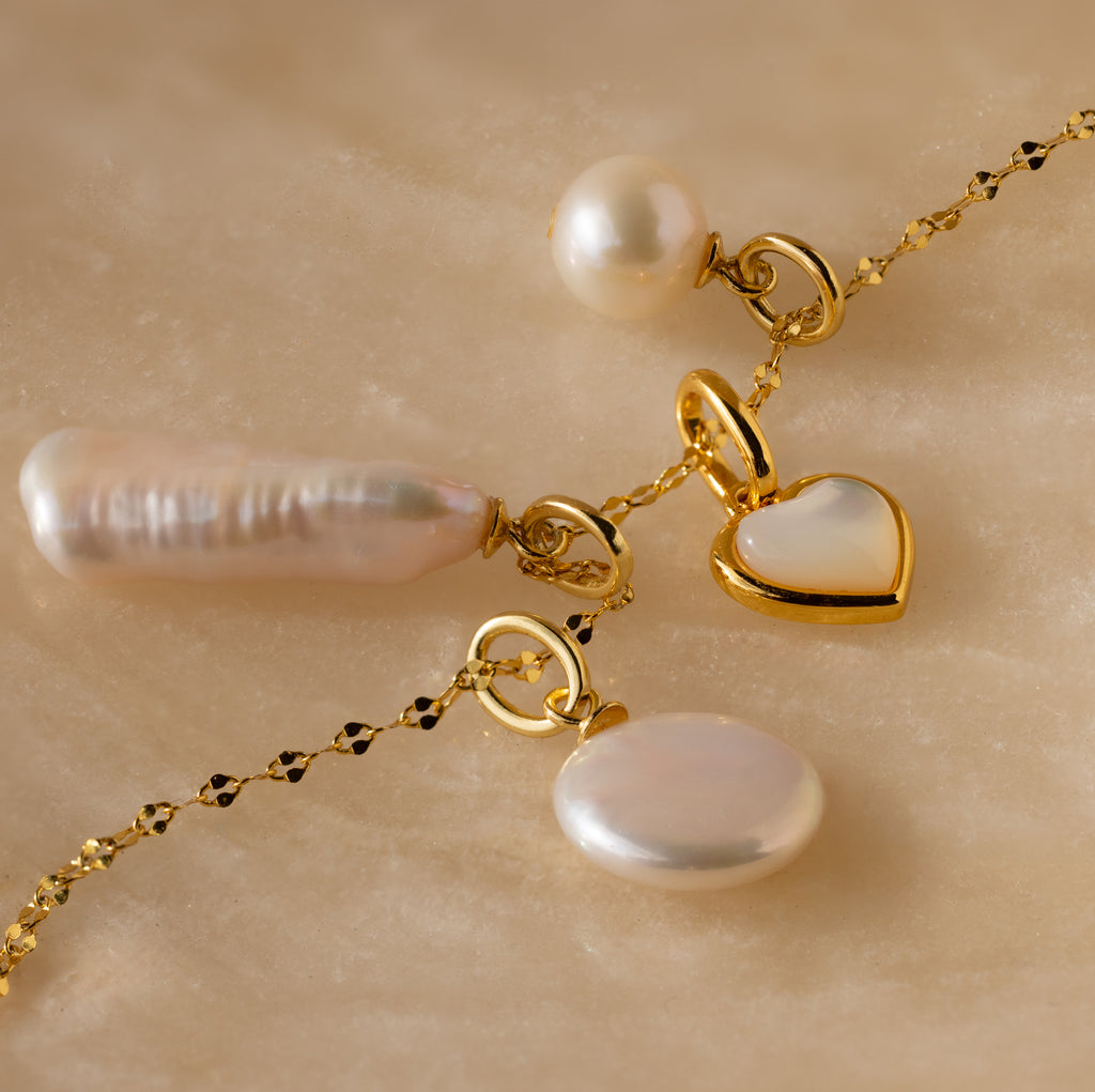 The Round Pearl Charm in 18K Gold is elegantly displayed on a marble surface.