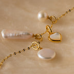 The Round Pearl Charm in 18K Gold is elegantly displayed on a marble surface.