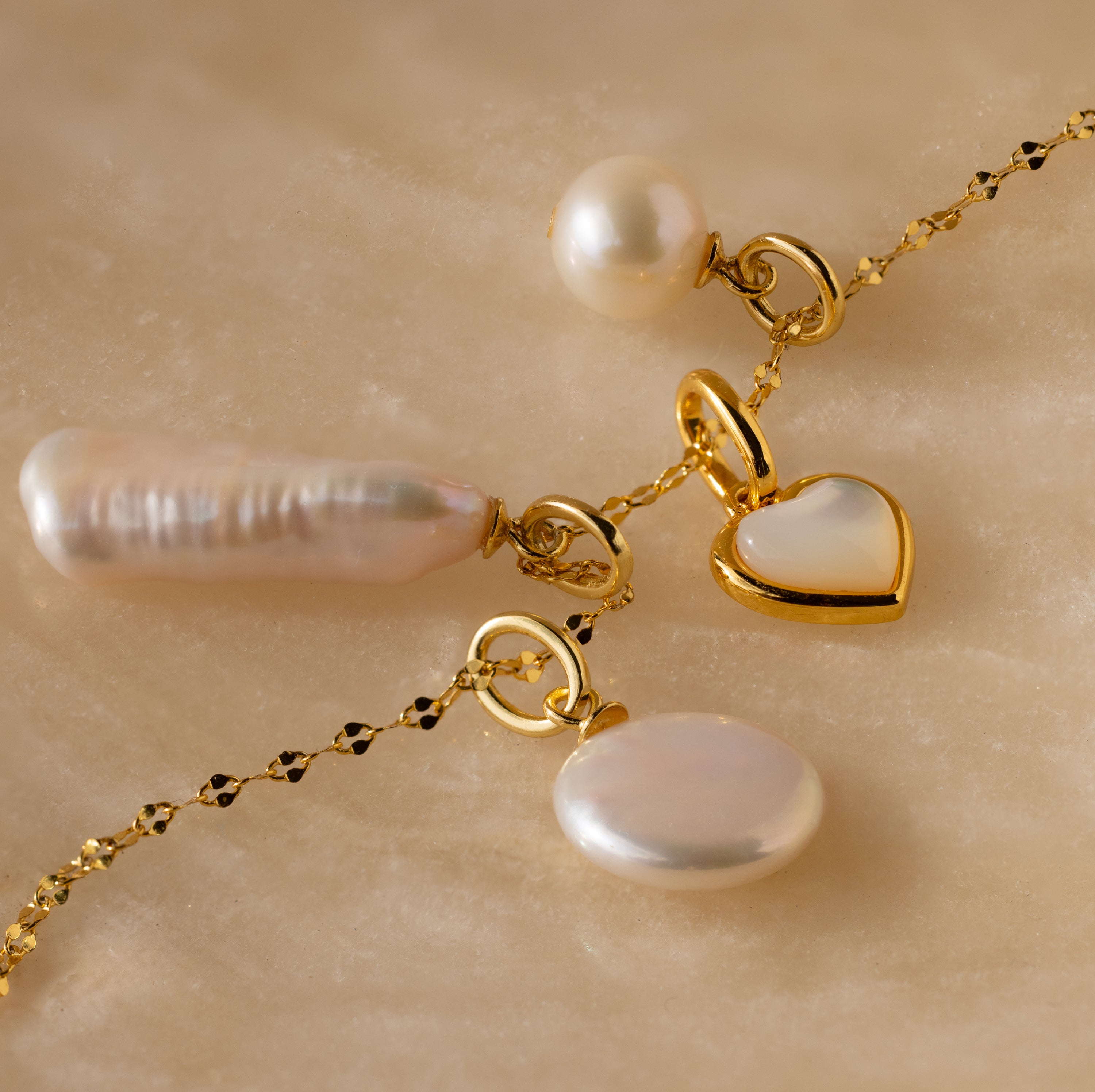The Round Pearl Charm in 18K Gold is elegantly displayed on a marble surface.