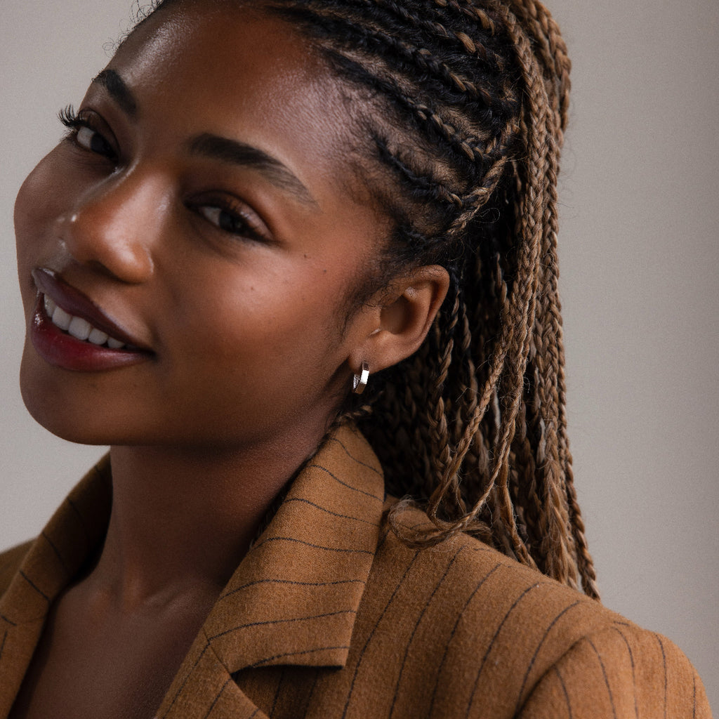 Woman with braided hair wearing a silver hoop earring and a brown pinstripe blazer against a neutral background