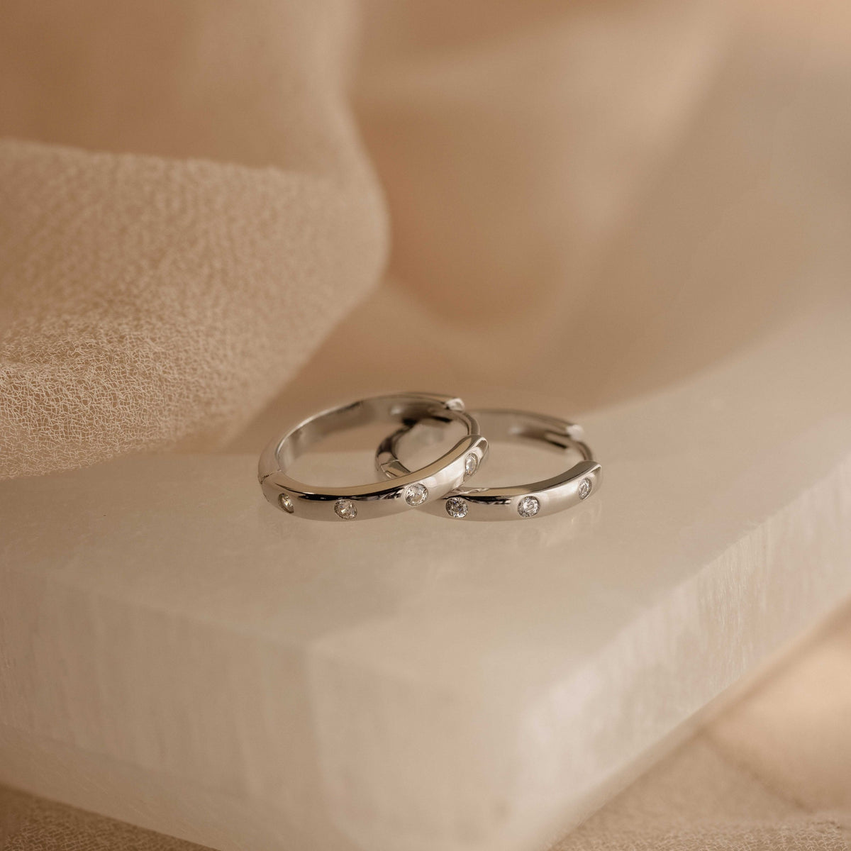 Classic Diamond Sprinkle Huggies rresting on a beige stone slab with soft draped fabric in the background.