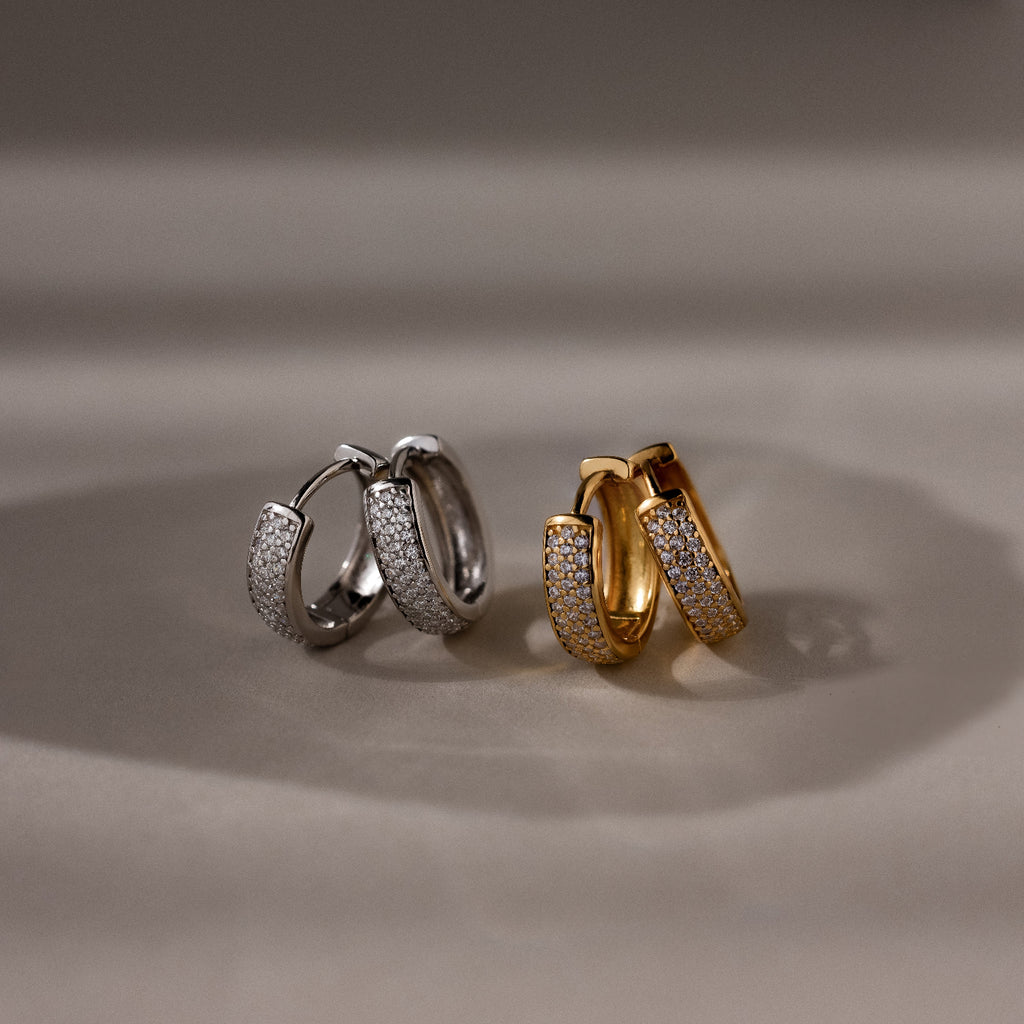 Pair of silver and gold hoop earrings on a reflective surface