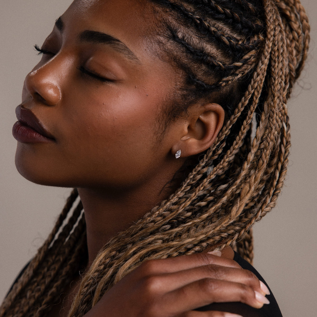 Woman with braided hair wearing a silver diamond earring against a neutral background