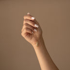 A manicured hand holds the Kinn Body Necklace—a gold body pendant—showcasing this elegant statement jewelry against a beige background.