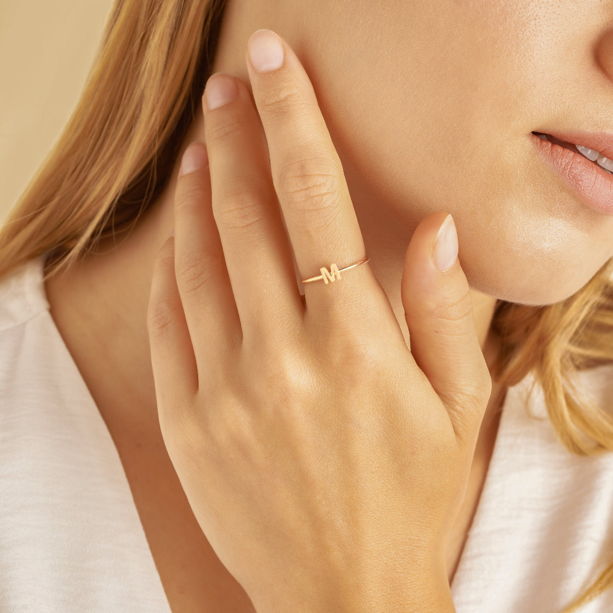 Close-up of a hand wearing a gold ring with a letter design, against a neutral background.
