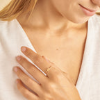 Close-up of a hand wearing a gold ring with a small letter on a white background
