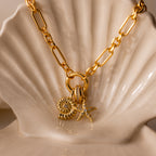 The Pave Dome Charm in 18K Gold adds sparkle, shown stacked with flower and starfish charms on a gold chain necklace, displayed on a white ceramic shell dish.