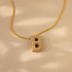 Pave Puff Letter Necklace in 18K Gold featuring a diamond-studded letter B pendant, displayed on a beige background with soft shadows.