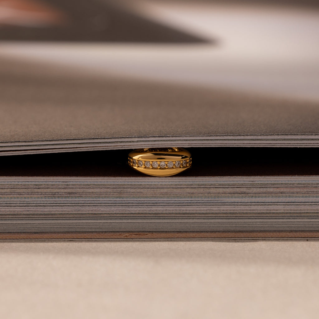 The Pave Dome Charm in 18K Gold adds sparkle as it rests between the pages of a closed book.