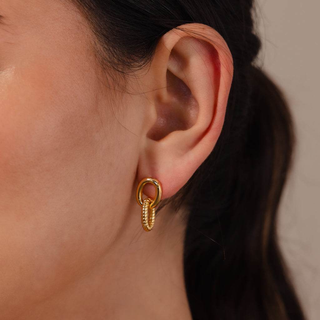 Close-up of a woman's ear wearing Twisted Link Earrings in 18K Gold—small, modern double-hoop earrings with a textured design for an elegant touch.